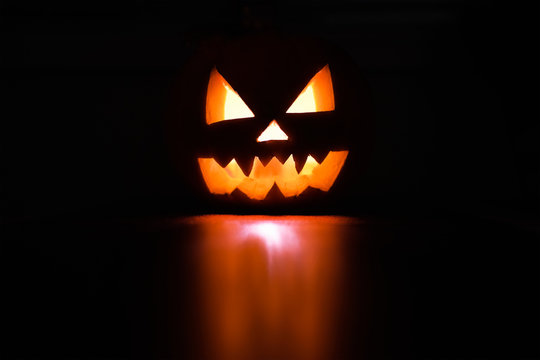 Halloween October holiday celebration symbol, scary pumpkin glowing with reflection, black background