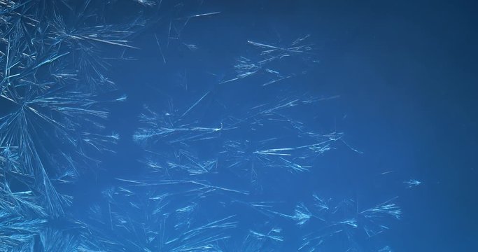 Blue winter background of ice crystals forming and frost freezing on window glass