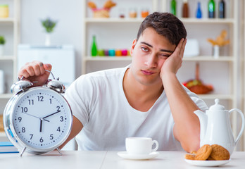 Man with alarm clock falling asleep at breakfast