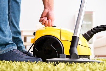 Man cleaning the floor carpet with a vacuum cleaner close up