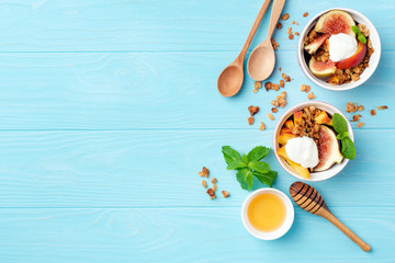 Healthy breakfast or snack figs peach yogurt granola in bowl on blue wooden background. Top view,...