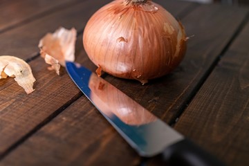 Onion laying on wooden table with a steel knife laying beside it. Reflection of onion on the knife