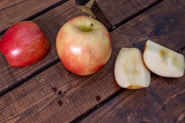 Slicing an apple with a knife and apple seeds laying on wooden background with slices of the apple stacked on each other for a healthy snack