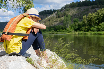 teenager girl dreams sitting on a stone shore. girl sitting in a life jacket near the water, river,...