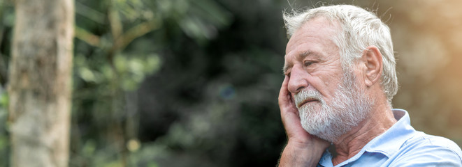Lonely senior man sitting on park bench. Caucasian man. Thinking about the past. Web banner frame.