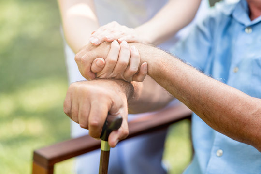 Caring nurse helping senior man sitting on bench in gaden. Asian woman, caucasian man. Holding hands with cane, close up. With light leaks.