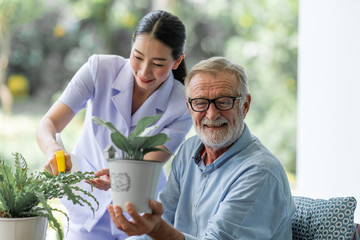 Senior man taking care of his plants with nurse. White man, asian woman. Happy smile.