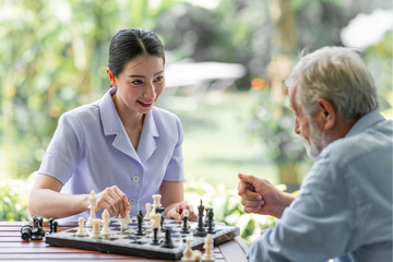 Young nurse playing chess with senior man. White male with asian woman. Concentrating.