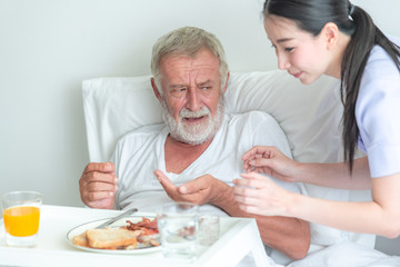 Senior man in bed having medication with nurse. Caucasian man with asian woman.  Dont want to take a pill.
