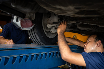 Asian Mechanic repairing a lifted car. Fixing car. Balancing the tire of the car. A car is lifting to let the Asian mechanic diagnostics the suspension of the vehicle to fix or repair it.