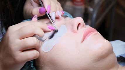 Young woman undergoing eyelash extension procedure in beauty salon, closeup