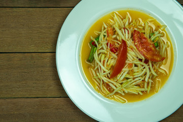 Most popular Thai street food yummy spicy papaya salad with green beans and tomatoes in white dish on wooden table background.