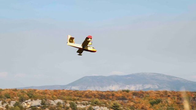 yellow Canadair CL-415 flying down in a valley to recharge