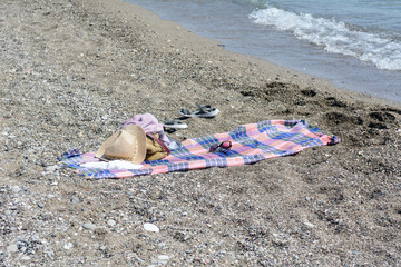 On the bedspread on the shore near the sea lie a bedspread, a straw hat, sunglasses, flips flop. Concept - beach vacation. Holidays at sea