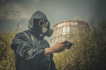 Man in gas mask is looking on mobile device in his hand with a test result of air pollution on a...