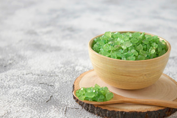 Green salt in wooden bowl and spoon, stand on gray concrete table. Spa, cosmetology, healthcare concept. Close-up, soft focus, copy space