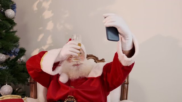 Santa Claus drinking a glass of beer while using his cellphone. Rest time. Alcoholic drink at the holidays. Drink with moderation. Craft beer. Merry Christmas. Cinematic 4K.