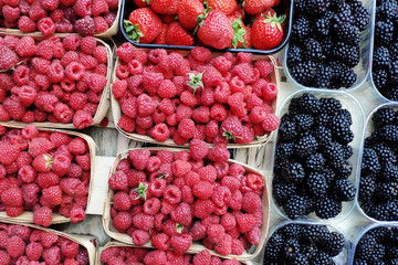 Fresh raspberries, strawberries and blackberries in plastic containers at the farmer's market. Natural organic food for a healthy diet.