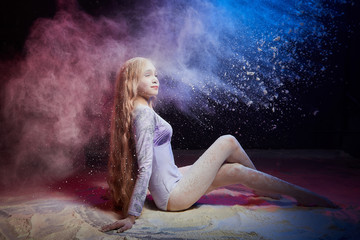 Fototapeta na wymiar Beautiful teen girl with long blonde curly hair in a dark room with colored lights and clouds of flour
