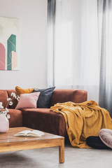 Yellow blanket on brown corner sofa in trendy living room interior