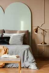 Golden lamp on modern nightstand table next to blue bed in grey bedroom interior