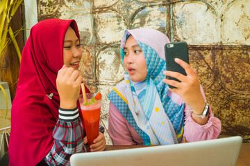 Obraz na płótnie Canvas young happy and beautiful Muslim student women in traditional Islamic hijab head scarf talking online business working together at cafe with laptop computer
