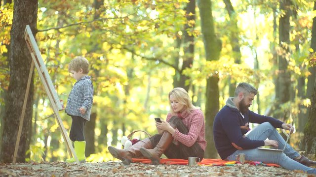 Happy child artist drawing picture on autumn nature. Happy mother father and son in the autumn park. Cheerful family having picnic.