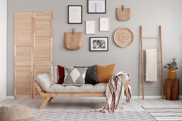 Wooden and wicker accessories in fashionable scandinavian living room interior with futon sofa with pillows - obrazy, fototapety, plakaty