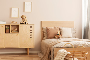 Stylish wooden commode with plush toy on top next to single bed in kid's bedroom