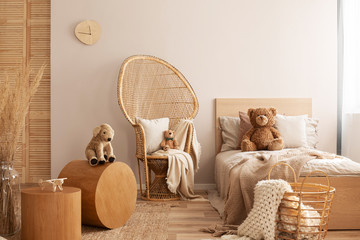 Wicker peacock chair with pillow, armchair and toy in beige and wooden baby bedroom interior