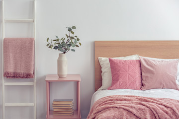 Pastel pink pillow and blanket on single wooden bed with white bedding in scandinavian bedroom interior