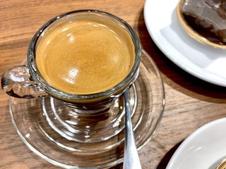  A cup of hot black coffee with bubbles in a glass cup with the light and shadow on wooden table background.