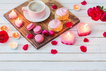 cup of coffee with cakes, candles and roses on white wooden back