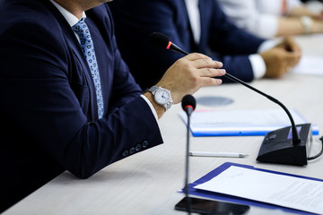 Details of a microphone, a man in a suit and expensive wrist watch at a press conference
