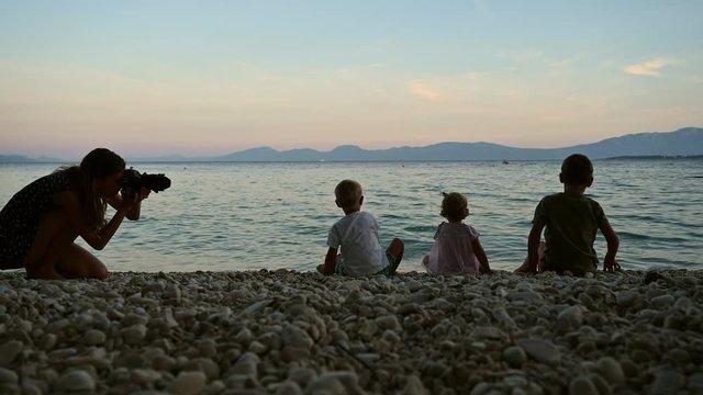 Professional photographer taking photos of three kids throwing pebbles in sea