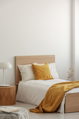 White and yellow bedding on single wooden bed in contemporary hotel interior