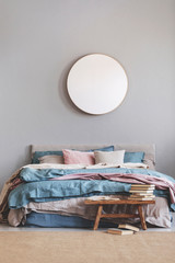 Round mirror in wooden frame on grey wall of elegant bedroom interior with comfortable bed with pastel, blue and pink bedding