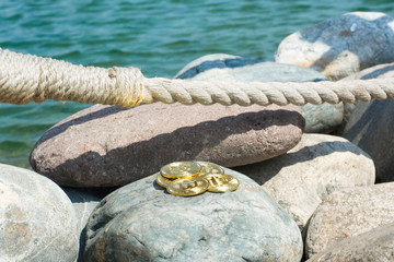 Fototapeta premium Bitcoin on sea stones, in background sea. Concept freelance, stock exchange.Background with copy space for text