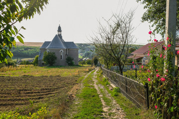 Footpath along the fence and plowed field to the church at the end of the street. The rural landscape of the village of Porokhova in Ukraine.
