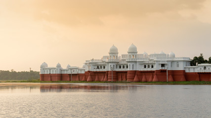 Evening sunset view of the lake place with red and white walls, beautiful domes and archways amid calm and serene water, Tripura, India