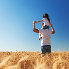 Happy father and daughter walk in the summer field. Nature beauty, blue sky and field with golden wheat. Outdoor lifestyle. Freedom concept.