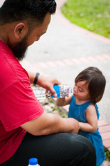 Bearded man gives water to a toddler child. Asian family, parenting and fatherhood concept.