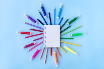 Back to school background with opened notepad and variety of school supplies in rainbow colors on pastel blue backdrop. Flat lay. Copy space.