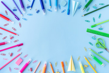 Variety of school supplies in rainbow colors on pastel blue background. Back to school concept. Flat lay. Copy space.