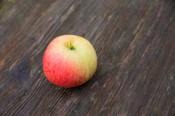 ein gelber rotbackiger Apfel auf einem alten dunkelbraunen Holztisch