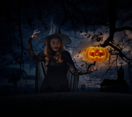 Halloween witch with pumpkin monster head over grass, dead tree, cross, birds, church and spooky cloudy sky, Halloween mystery concept