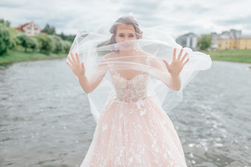 Beautiful  bride in wedding dress with veil over her face posing outdoor with lake on background.