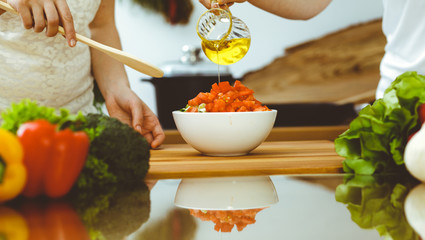 Closeup of human hands cooking in kitchen. Mother and daughter or two female friends cutting vegetables for fresh salad. Friendship, family dinner and lifestyle concepts