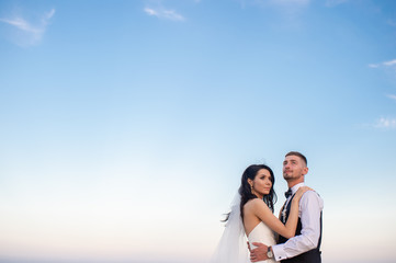 Beautiful bride hugging her groom with sky on background