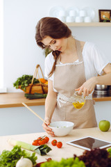 Young brunette woman cooking in kitchen. Housewife holding wooden spoon in her hand. Food and health concept